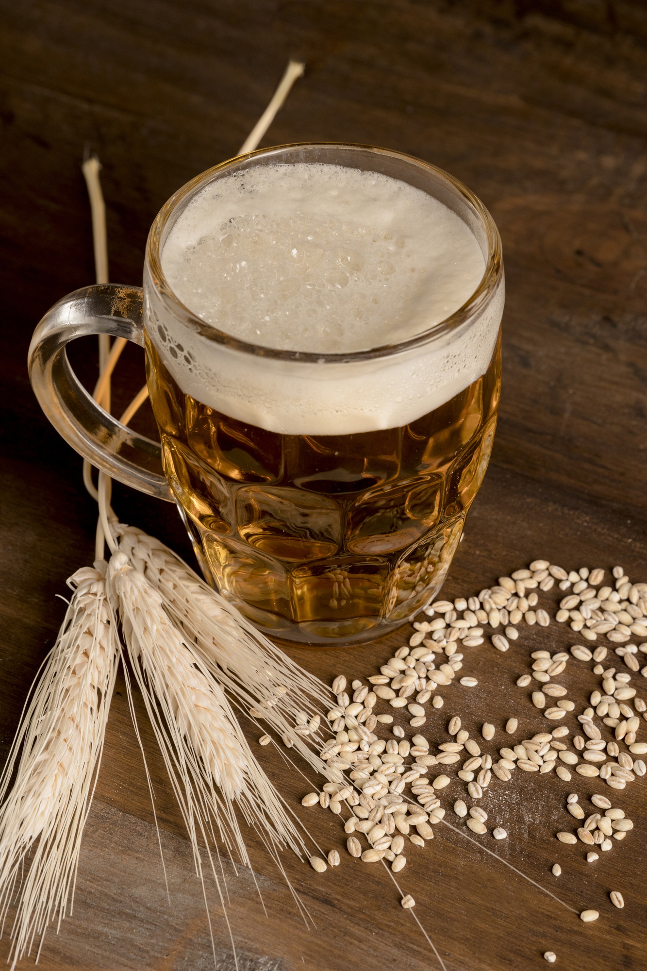 Grãos de malte claro ao lado de um copo de cerveja sobre madeira escura